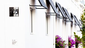 Eine Reihe moderner Hotelzimmer mit schwarzen Markisen, einer weißen Fassade und einem Schild, das einen barrierefreien Zugang anzeigt.