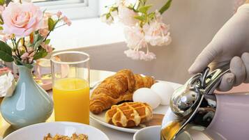 A breakfast tray with croissants, eggs, cereal, and orange juice.
