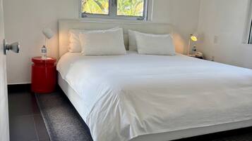 Ein Schlafzimmer mit einem Bett, einem Fenster, einem Nachttisch und einer roten Mülltonne.