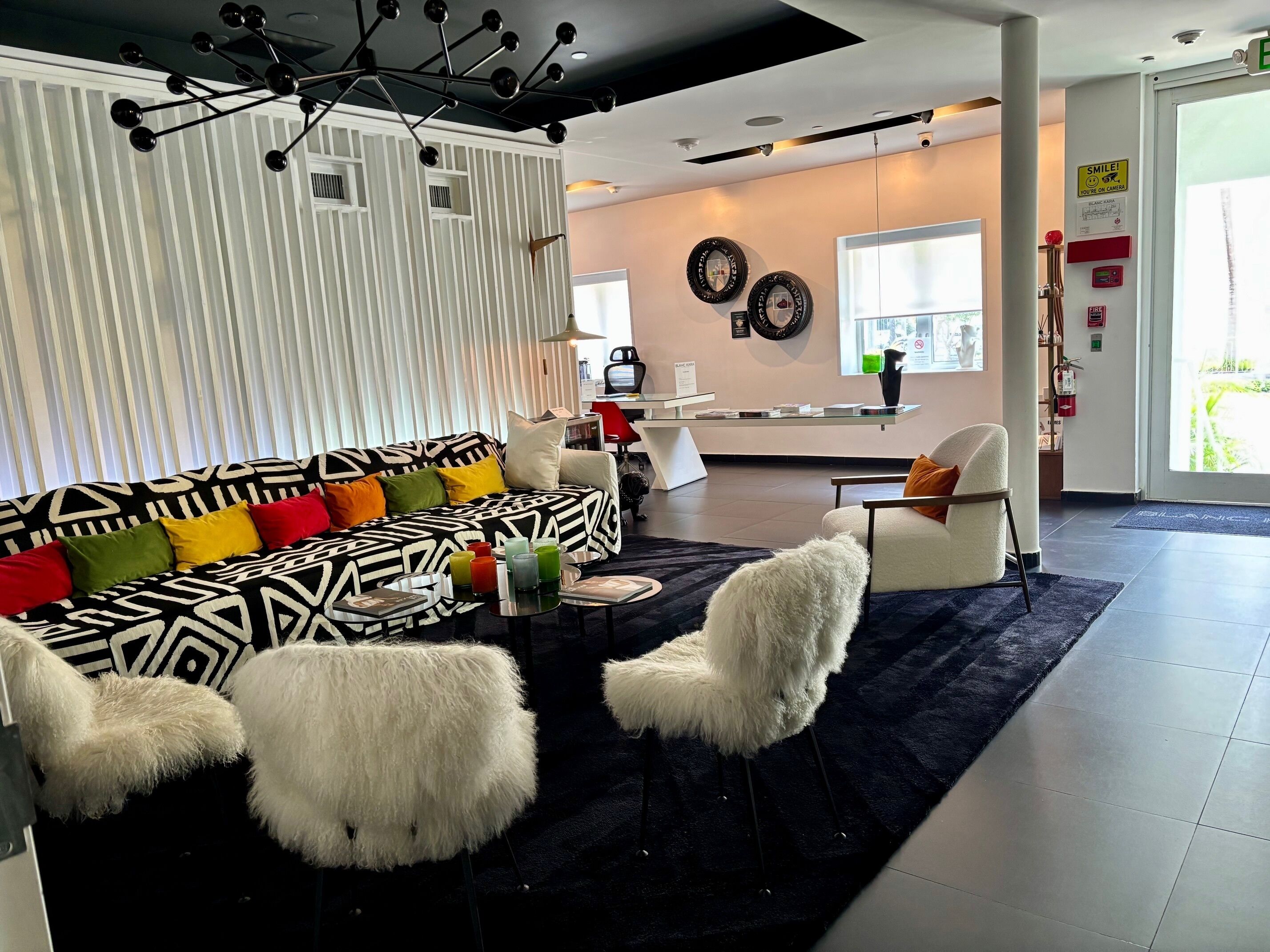 Una sala moderna con un sofá estampado, sillas blancas y mullidas, una mesa de centro con bebidas y un comedor al fondo.
