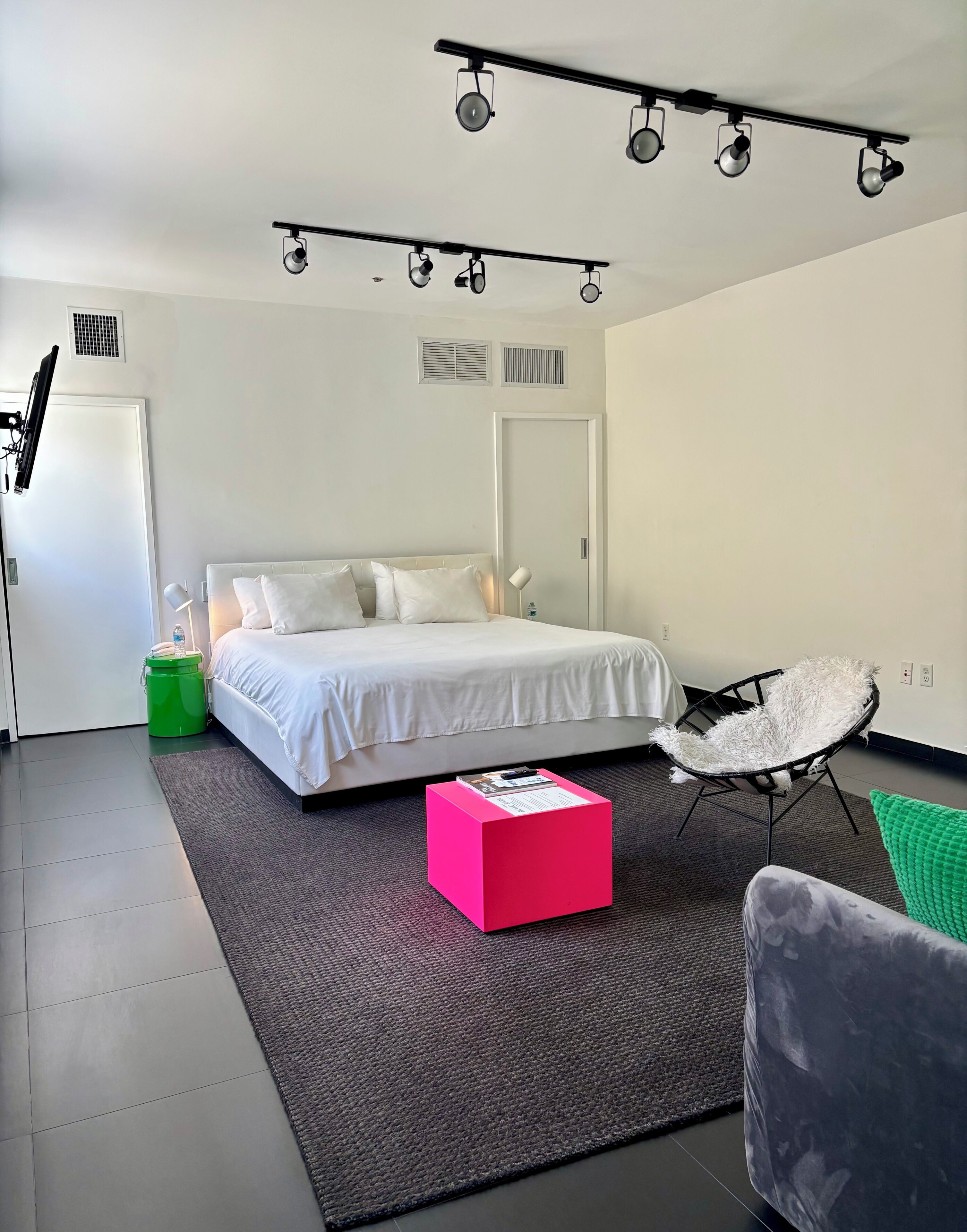 Ein modernes Schlafzimmer mit einem Bett, einem Schreibtisch, einem Stuhl und einer kleinen grünen Mülleimer.