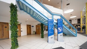 Moderni sisätila, jossa on sininen portaikko, vihreä pystysuora puutarja ja informatiiviset opasteet.