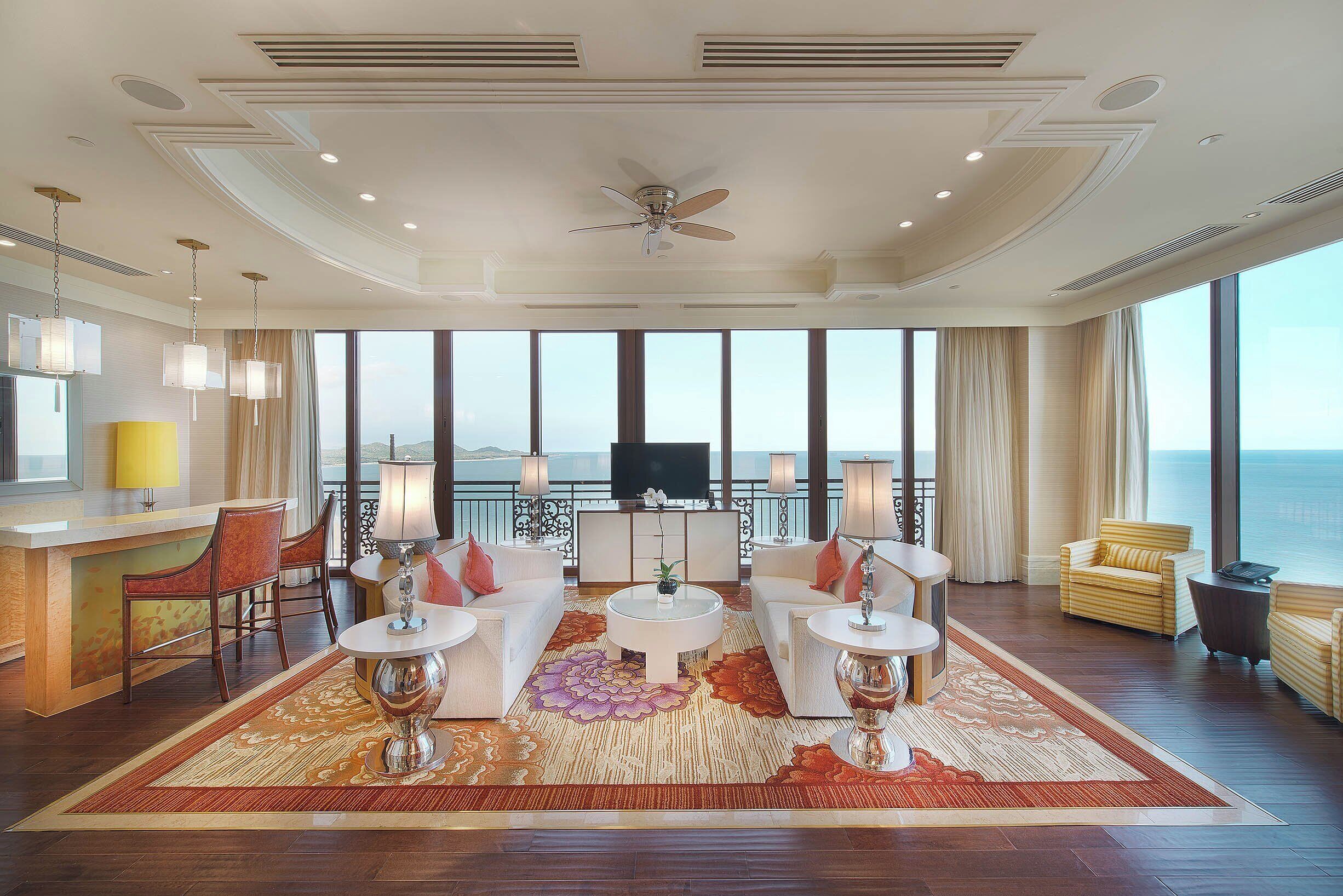 A spacious living room with a large window, a ceiling fan, and a central coffee table.