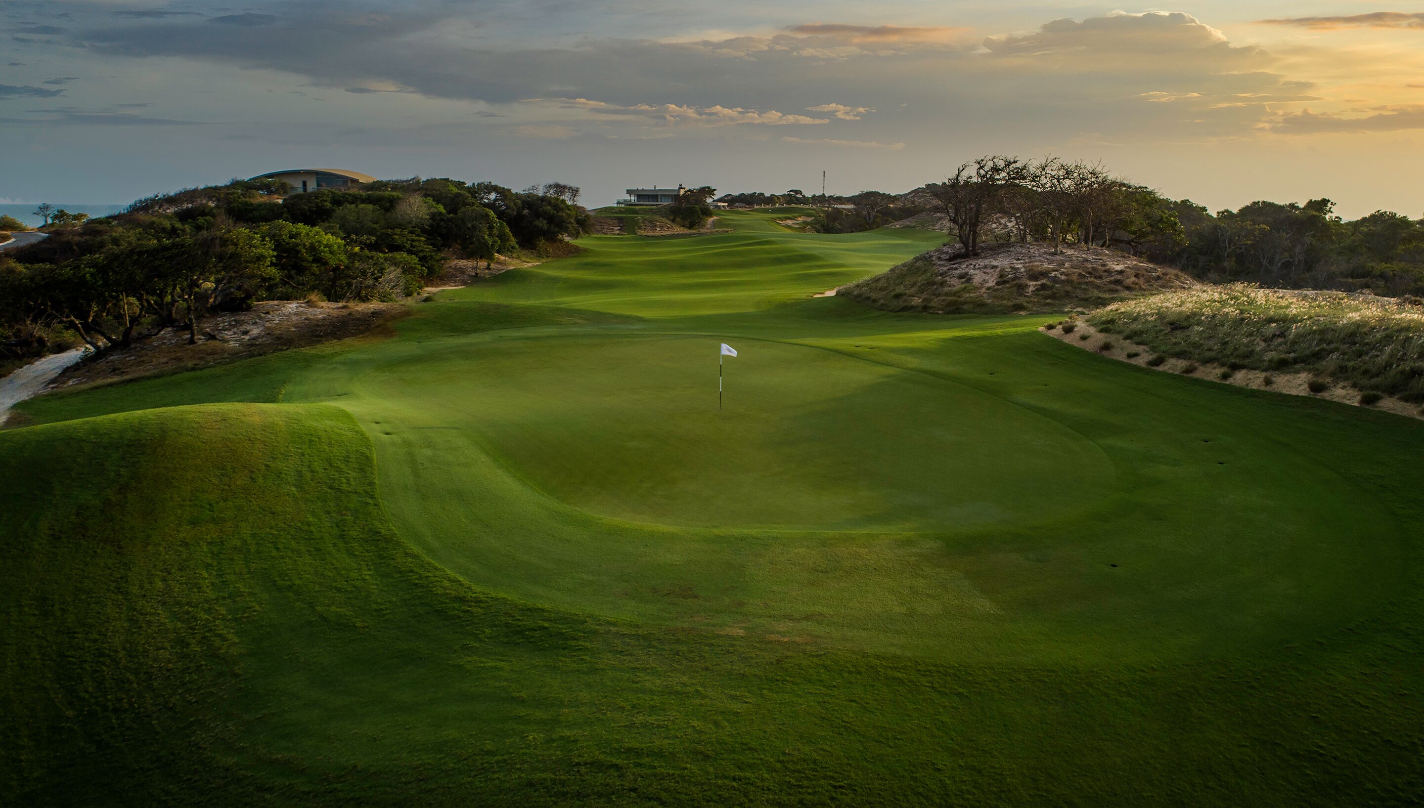 A golf course with a flagstick in the center, surrounded by well-maintained grass and sand bunkers.