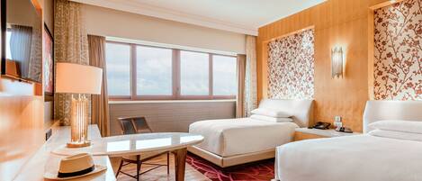 Una habitación de hotel con cama, escritorio con lámpara, silla y ventana con cortinas.