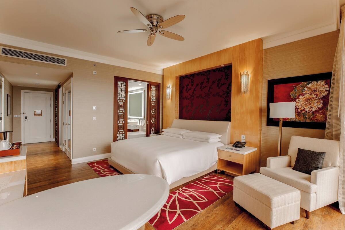 A hotel room with a bed, a desk, a chair, a round table, and a ceiling fan.