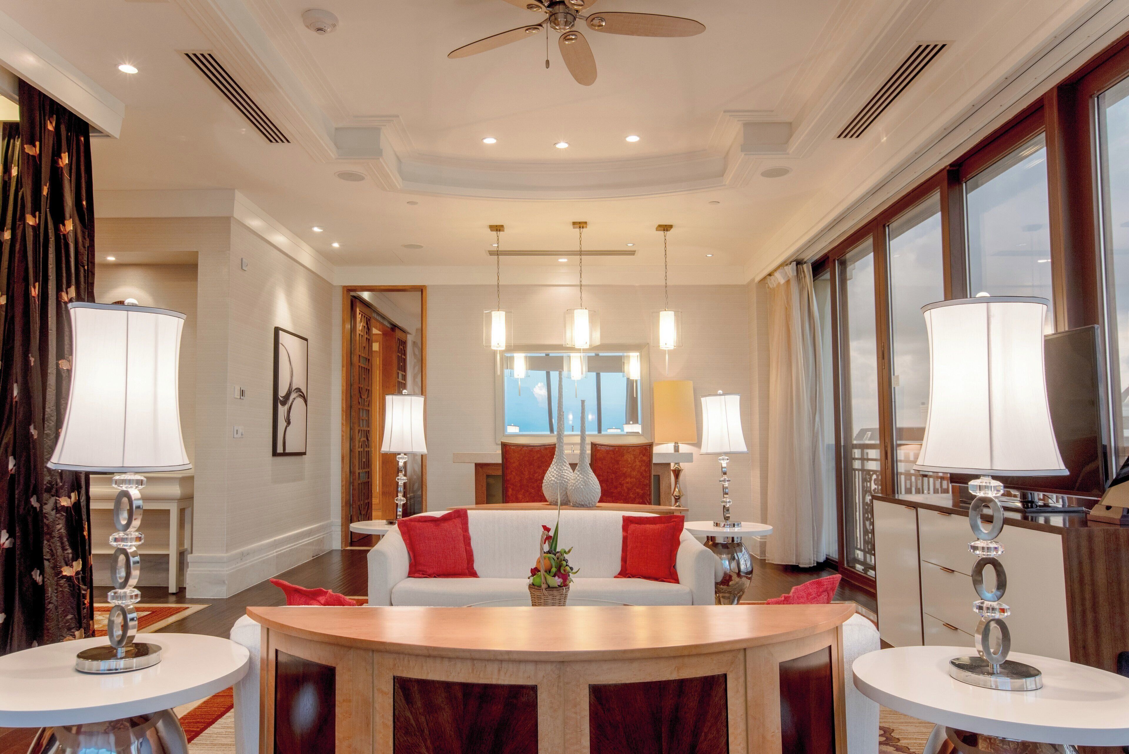 A hotel room with a large bed, a sitting area with a sofa and a table, and a view of the outdoors through the windows.
