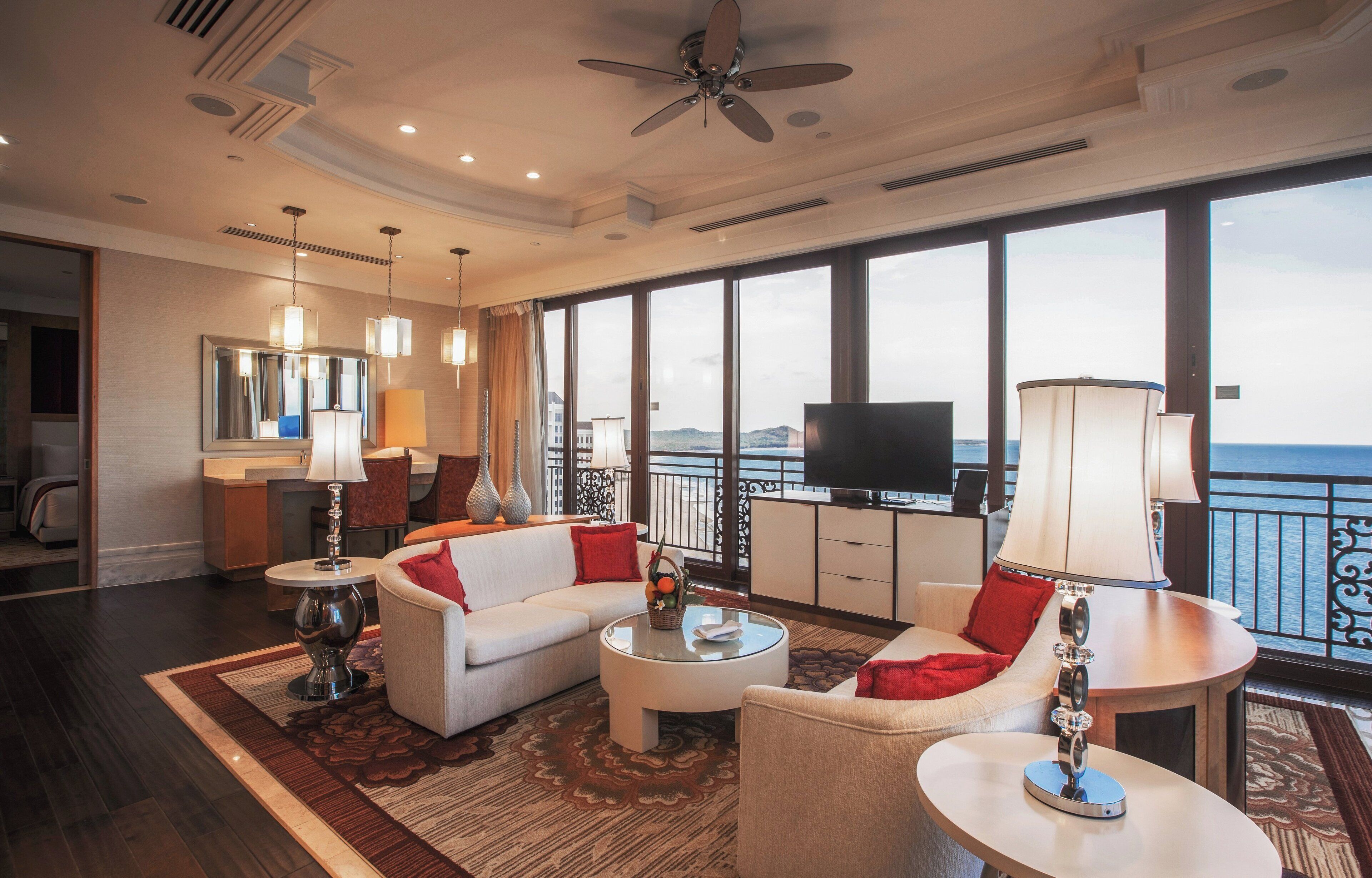 A spacious living room with a large television, comfortable seating, and a view of the sea.