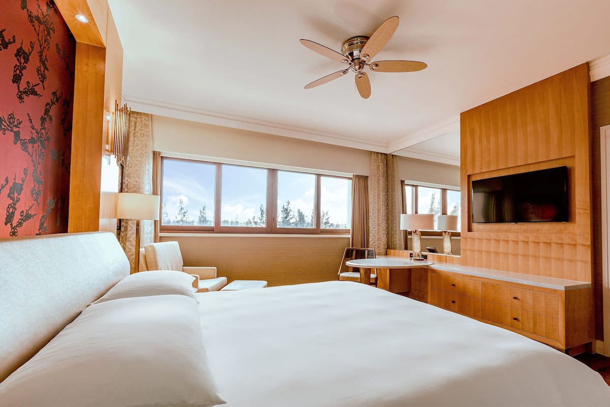 A hotel room with a large bed, a desk, a chair, a TV mounted on the wall, and a ceiling fan.