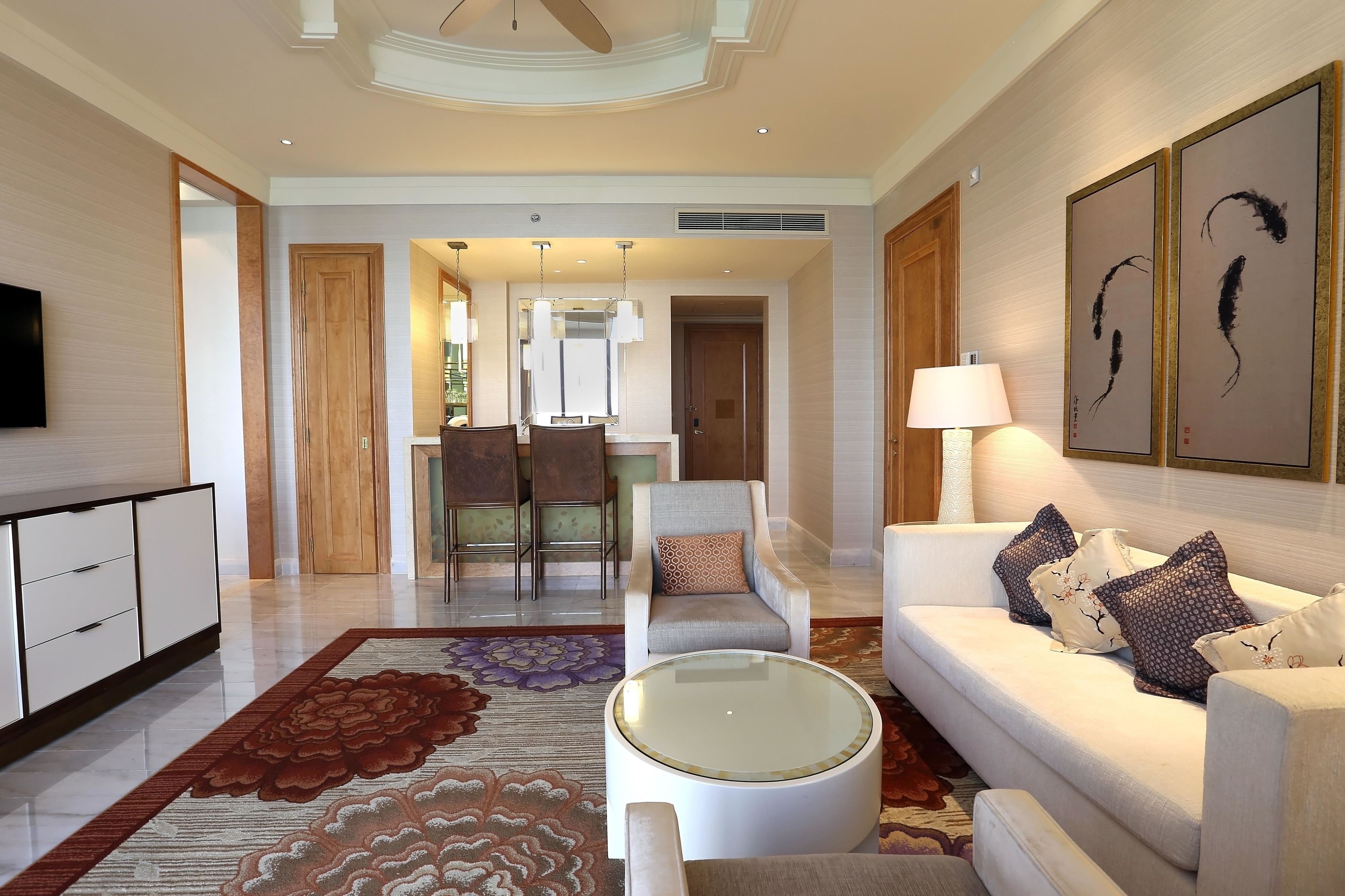 Un moderno vestíbulo de hotel con un sofá, un sillón y una mesa redonda. En el fondo, hay un área de comedor con una mesa y sillas.