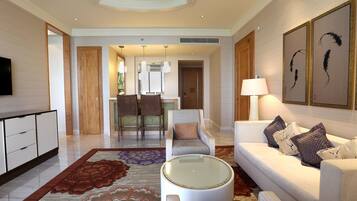 A modern hotel lobby with a sofa, armchair, and a round coffee table. There is a dining area in the background with a table and chairs.