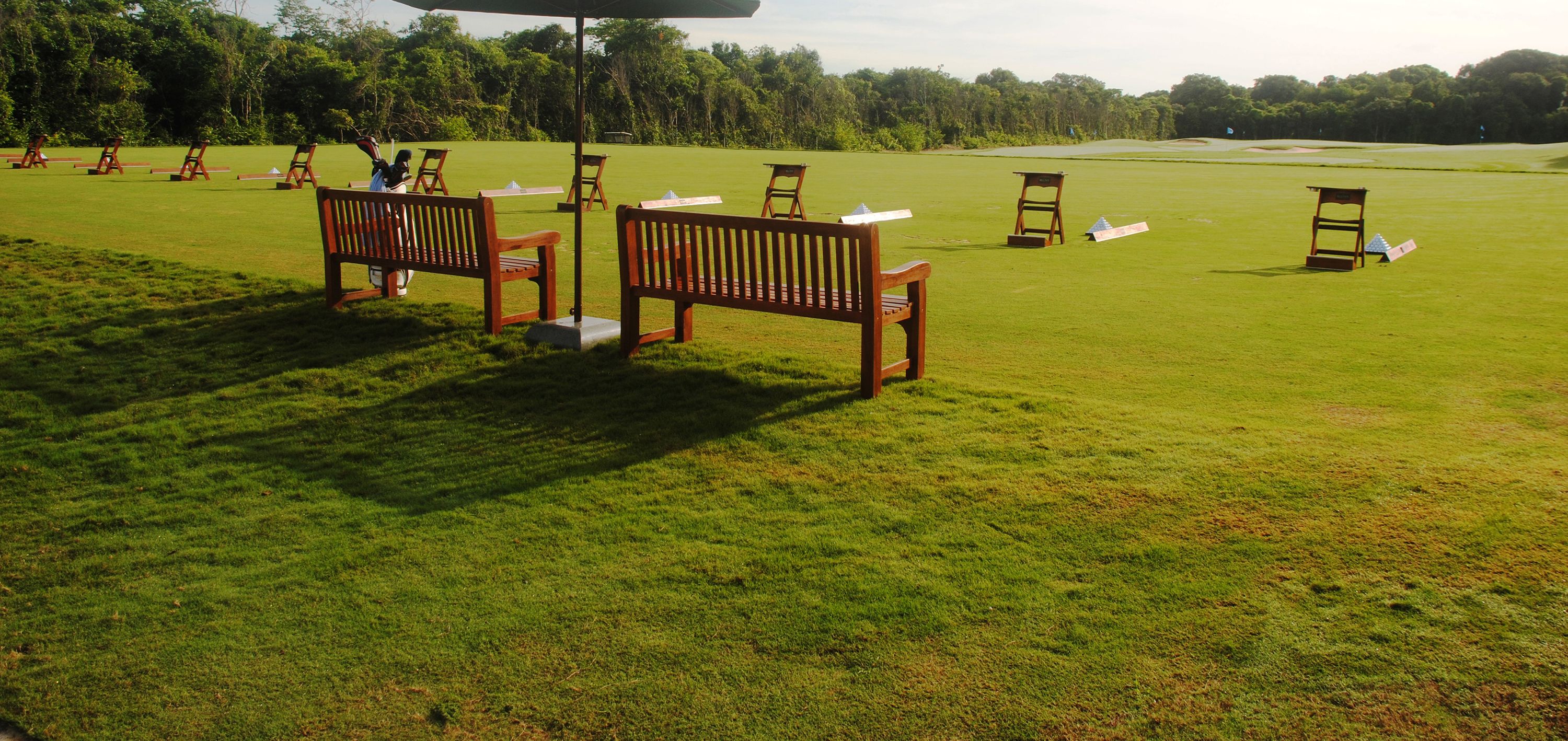 An outdoor seating area with wooden benches and tables, surrounded by a well-maintained lawn.