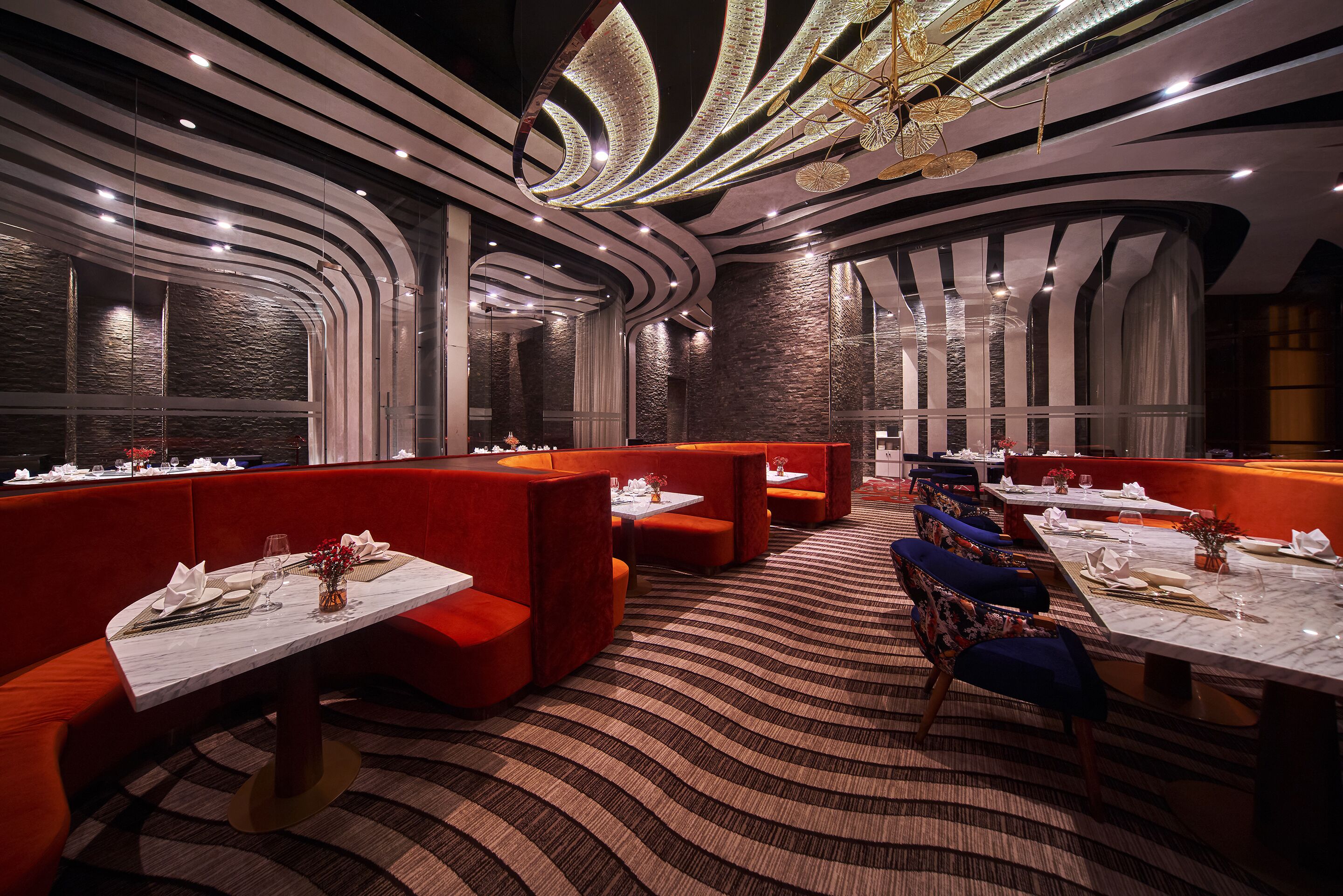 A modern restaurant with red booths, white tables, and a patterned carpet.