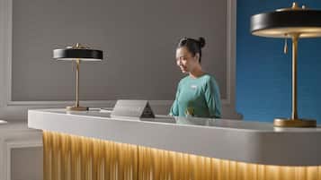 A reception desk with a nameplate labeled "CONCIERGE," a modern lamp, and a patterned wall in the background.