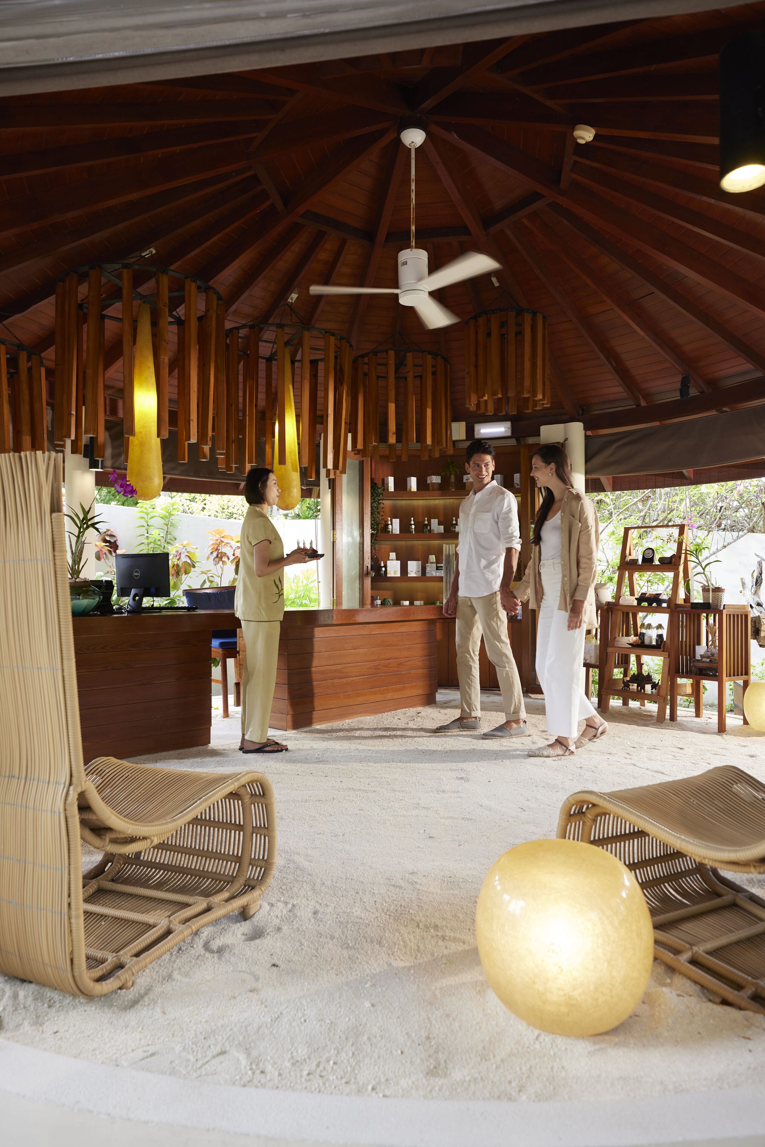 Un espacio al aire libre techado, con techo de madera, mobiliario de mimbre y un mostrador de recepción con plantas.