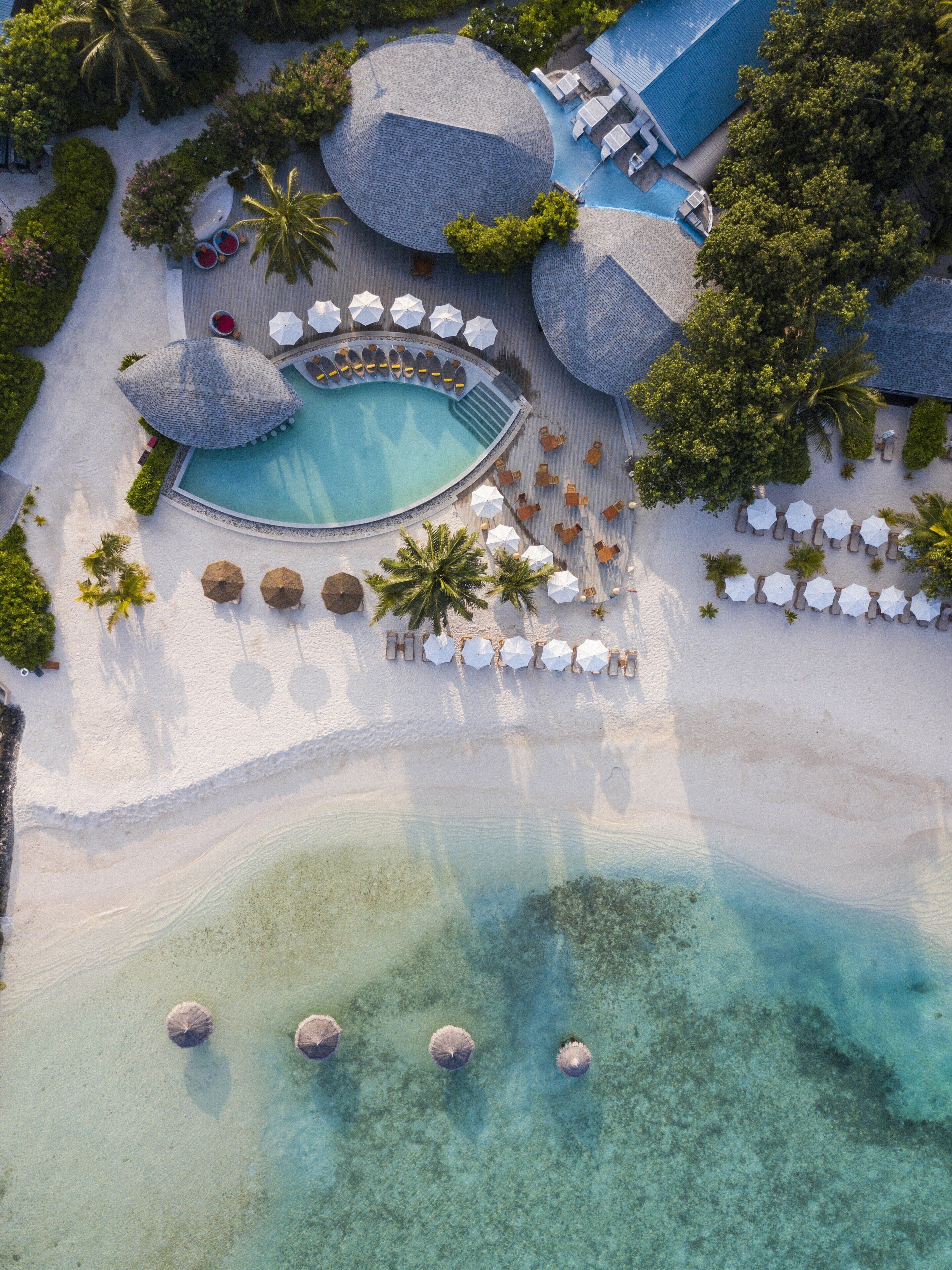 Vista aérea de un resort con piscina central, zonas de descanso y playa.
