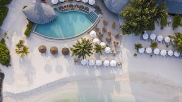 Vista aérea de un resort con piscina central, zonas de descanso y playa.