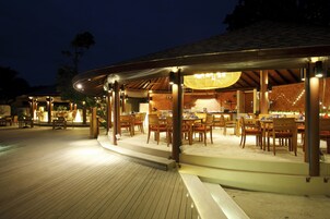 Un restaurante al aire libre con mesas y sillas de madera, una zona de estar cubierta y una terraza de madera.