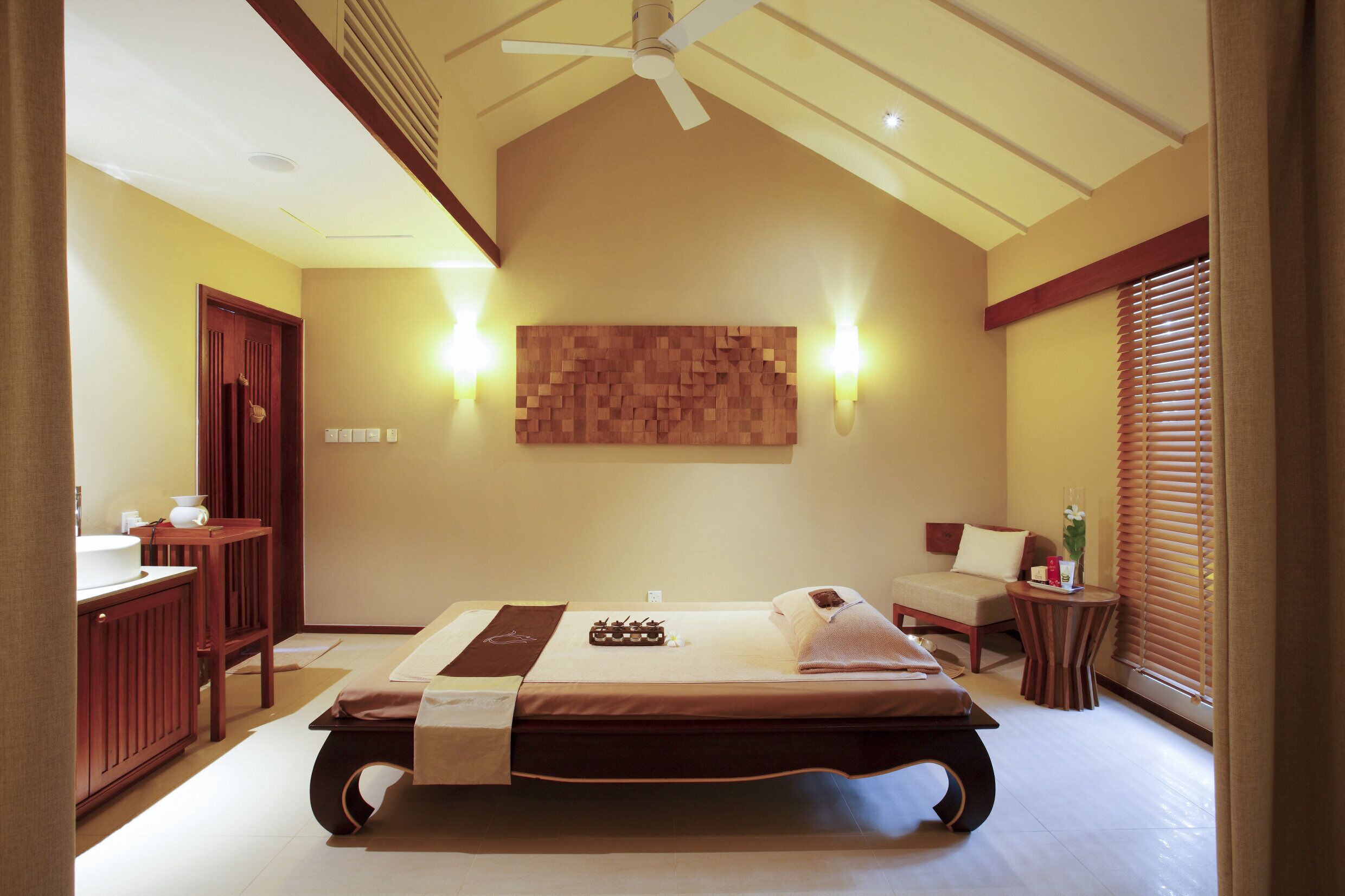A spacious bedroom with a large bed, a wooden headboard, a ceiling fan, and a wall-mounted artwork.