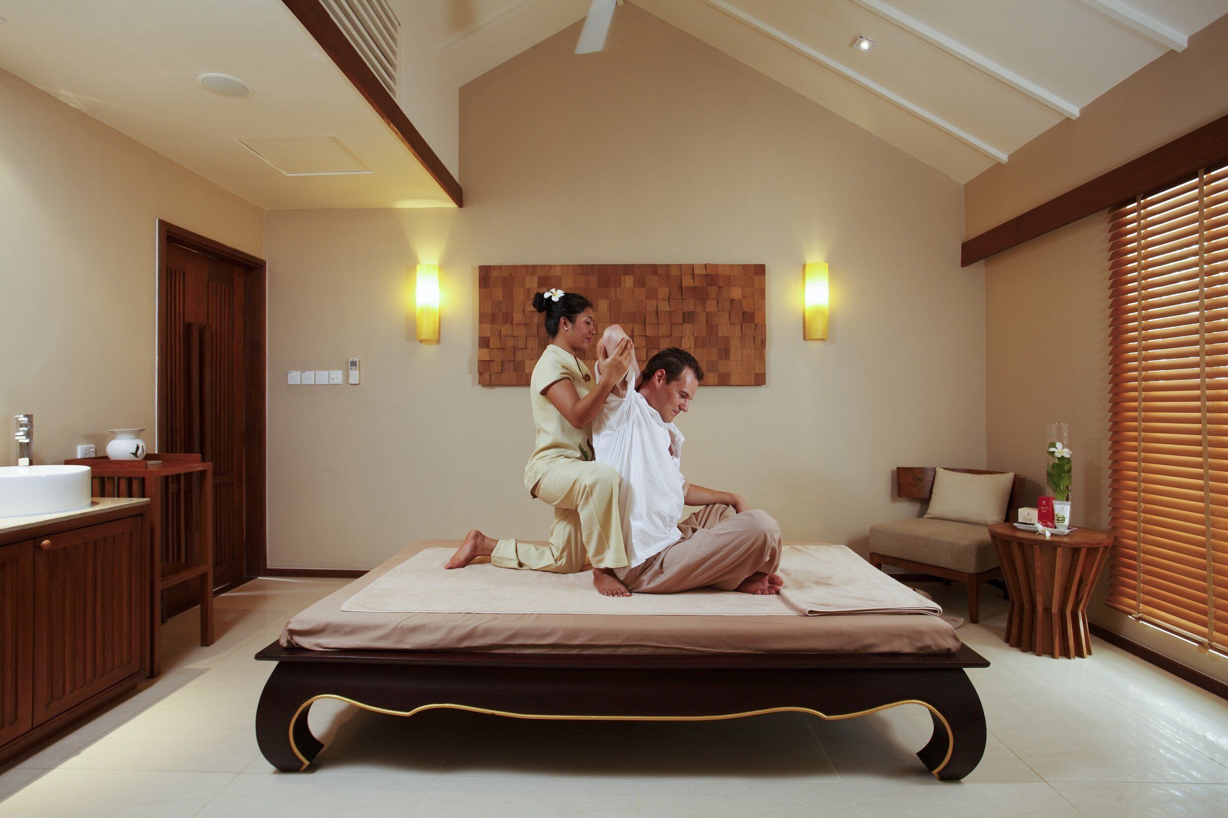 A room with a bed, a wooden cabinet, a small table, and a wall-mounted light fixture.
