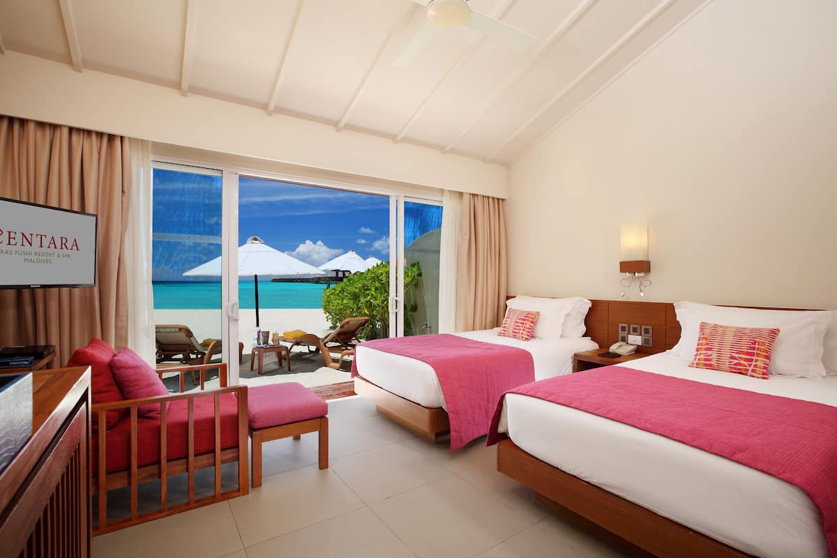 Habitación de hotel con dos camas, televisión, balcón con vista al mar y un letrero de Centara.