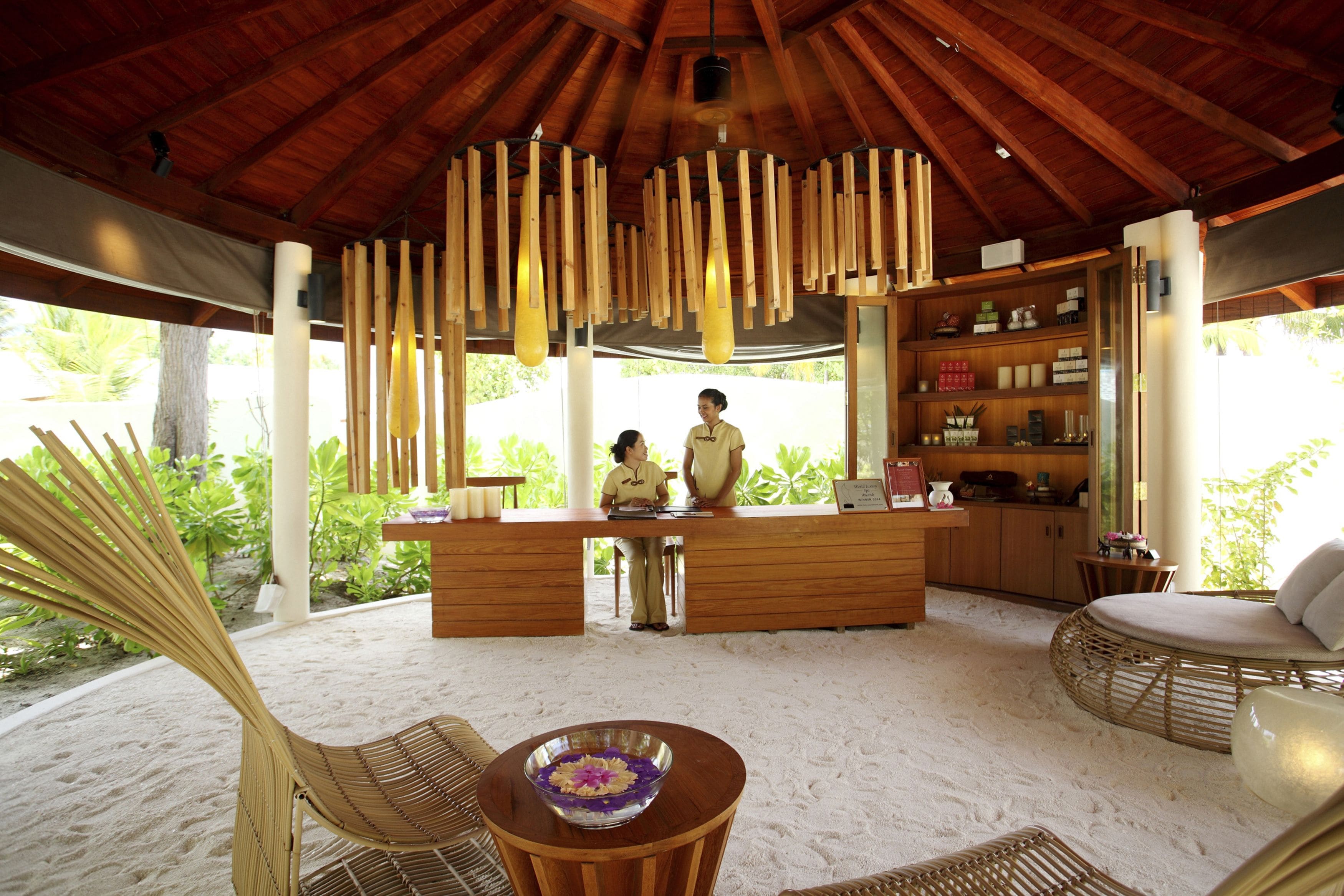 Un complexe hôtelier en bord de mer doté d’un comptoir d’accueil en bois, d’un bar et d’un espace détente avec un sol sablonneux.