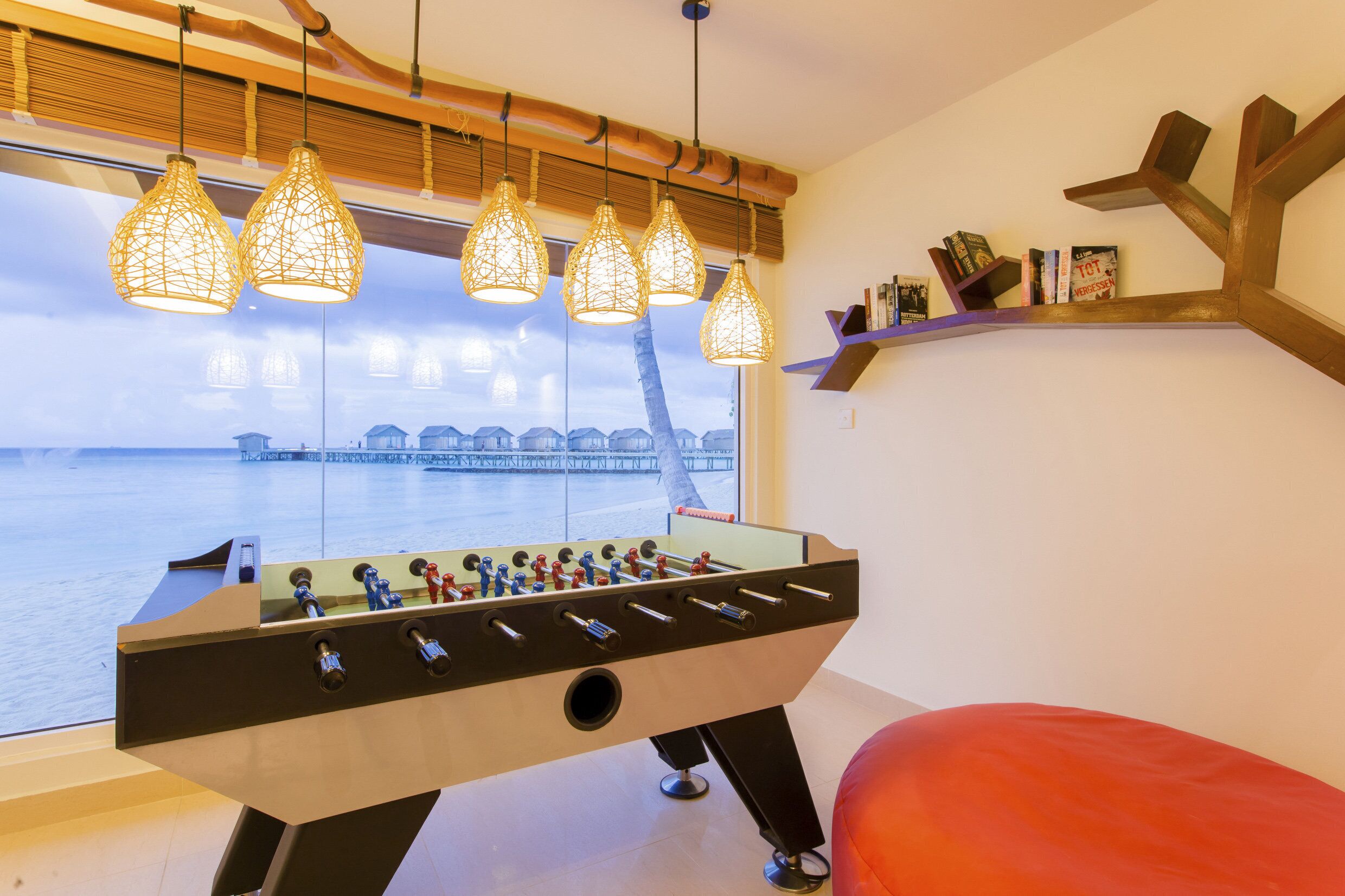 A foosball table in a room with a view of a body of water, wooden ceiling beams, and pendant lights.