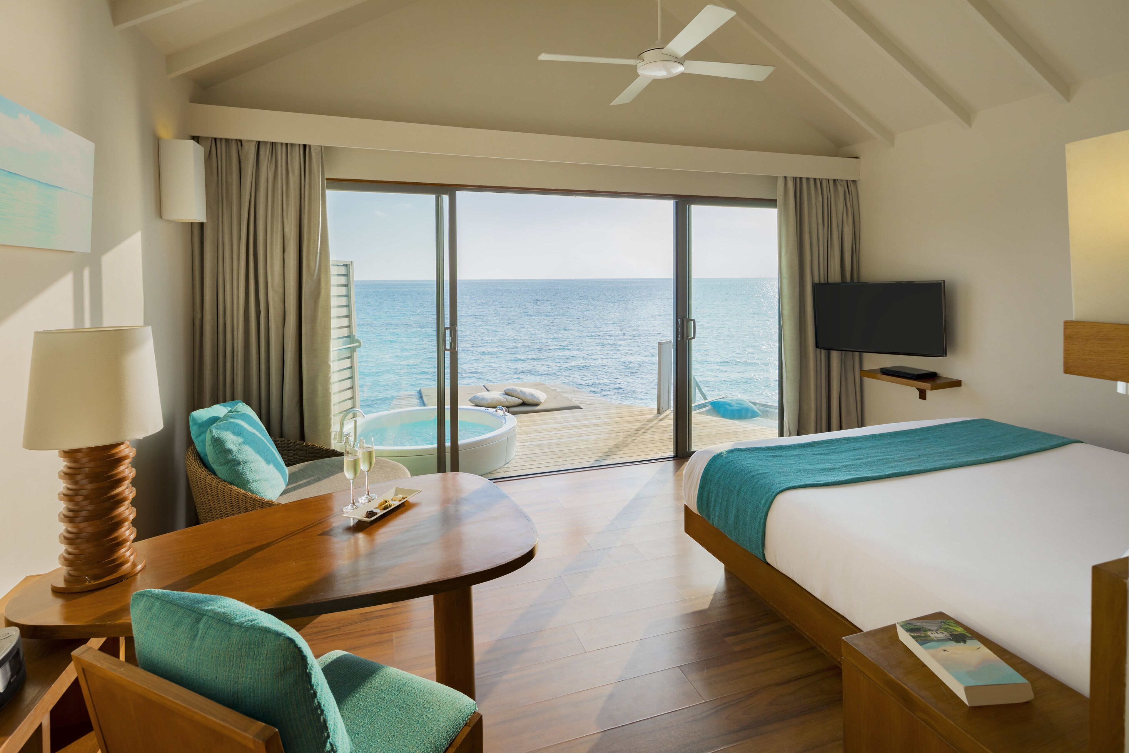 A hotel room with a bed, a desk, a chair, a television, and a view of the ocean.