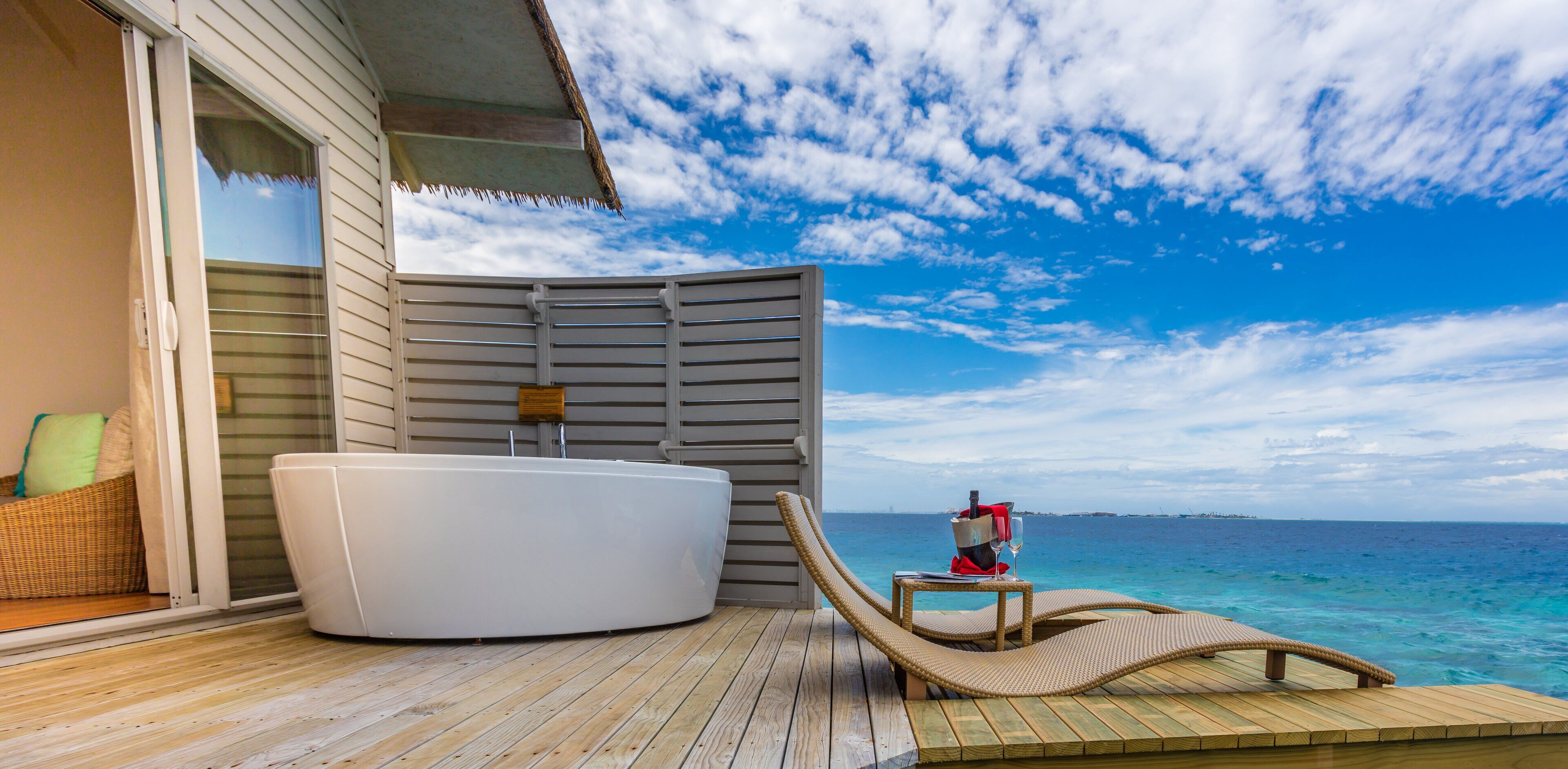 A wooden deck with a hot tub and a lounge chair facing the ocean.