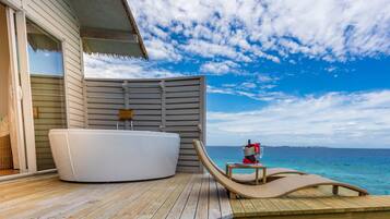 A wooden deck with a hot tub and a lounge chair facing the ocean.