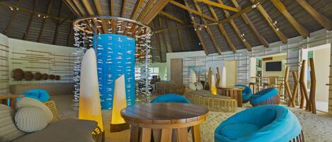 A spacious room with a high wooden ceiling, a central pillar with hanging decorations, and several seating areas including a round wooden table and two blue bean bag chairs.