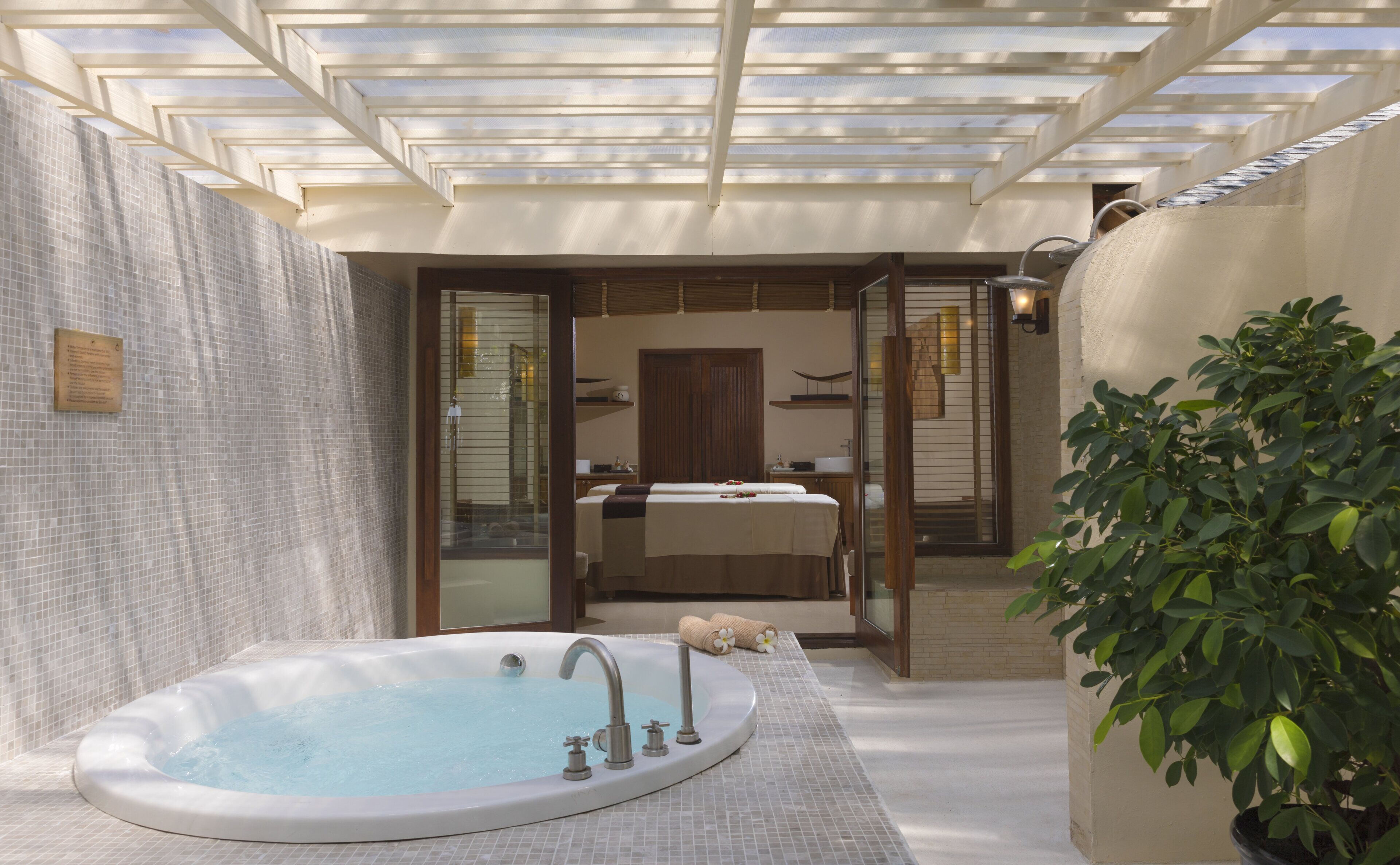 A spa area with a hot tub, a wooden bench, and a glass door leading to a bathroom.