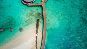 Vista aérea de un resort con bungalows sobre el agua, unidos por una pasarela de madera.