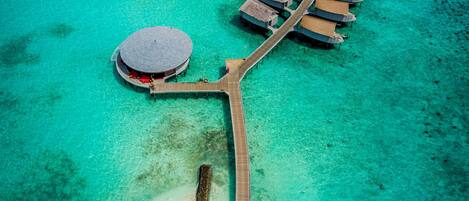 Vista aérea de un resort con bungalows sobre el agua, unidos por una pasarela de madera.
