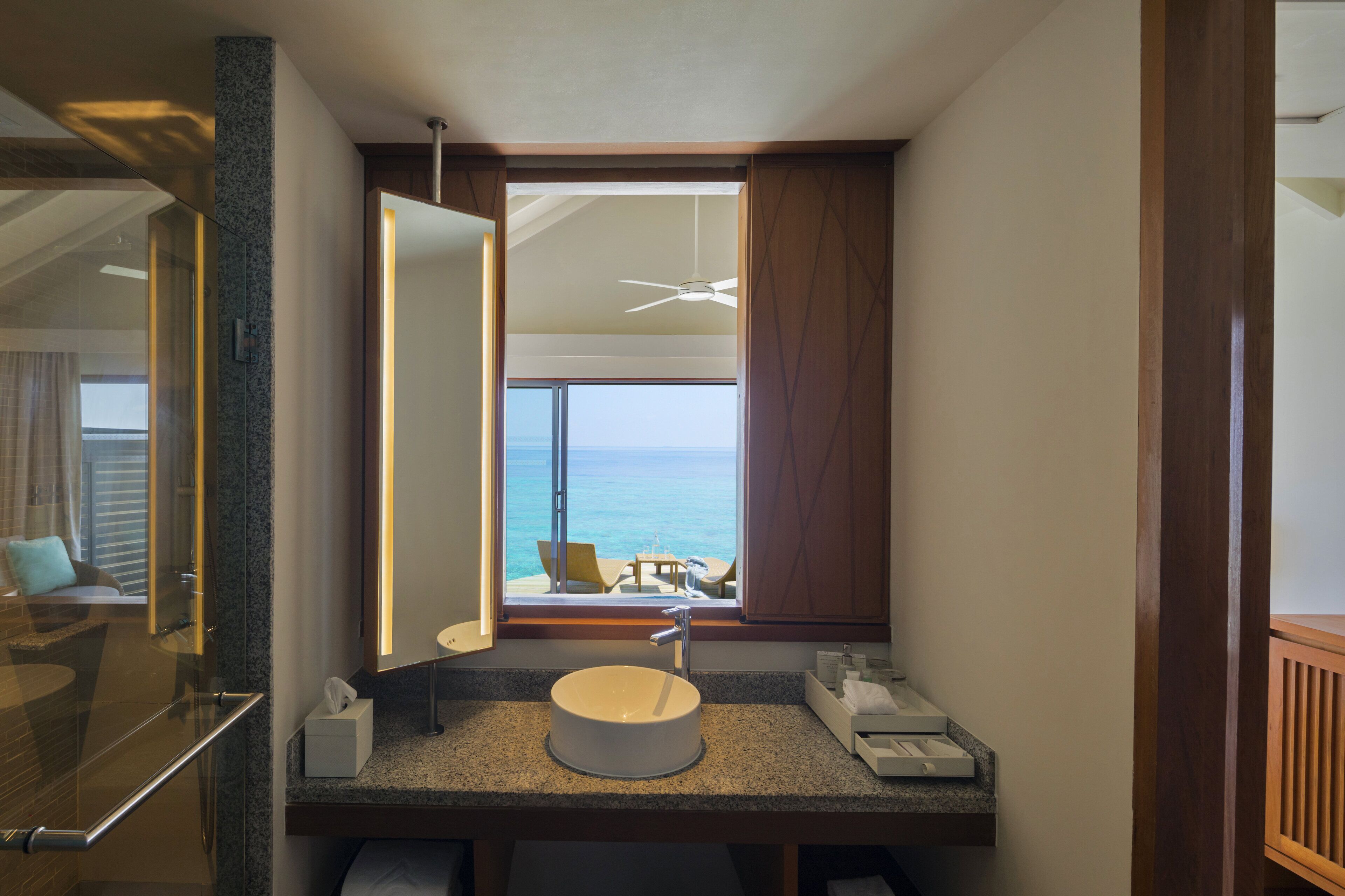 Une salle de bain avec un lavabo rond, un grand miroir et une vue sur la mer par une fenêtre.