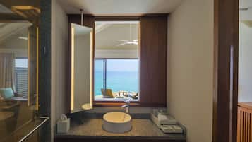 Une salle de bain avec un lavabo rond, un grand miroir et une vue sur la mer par une fenêtre.