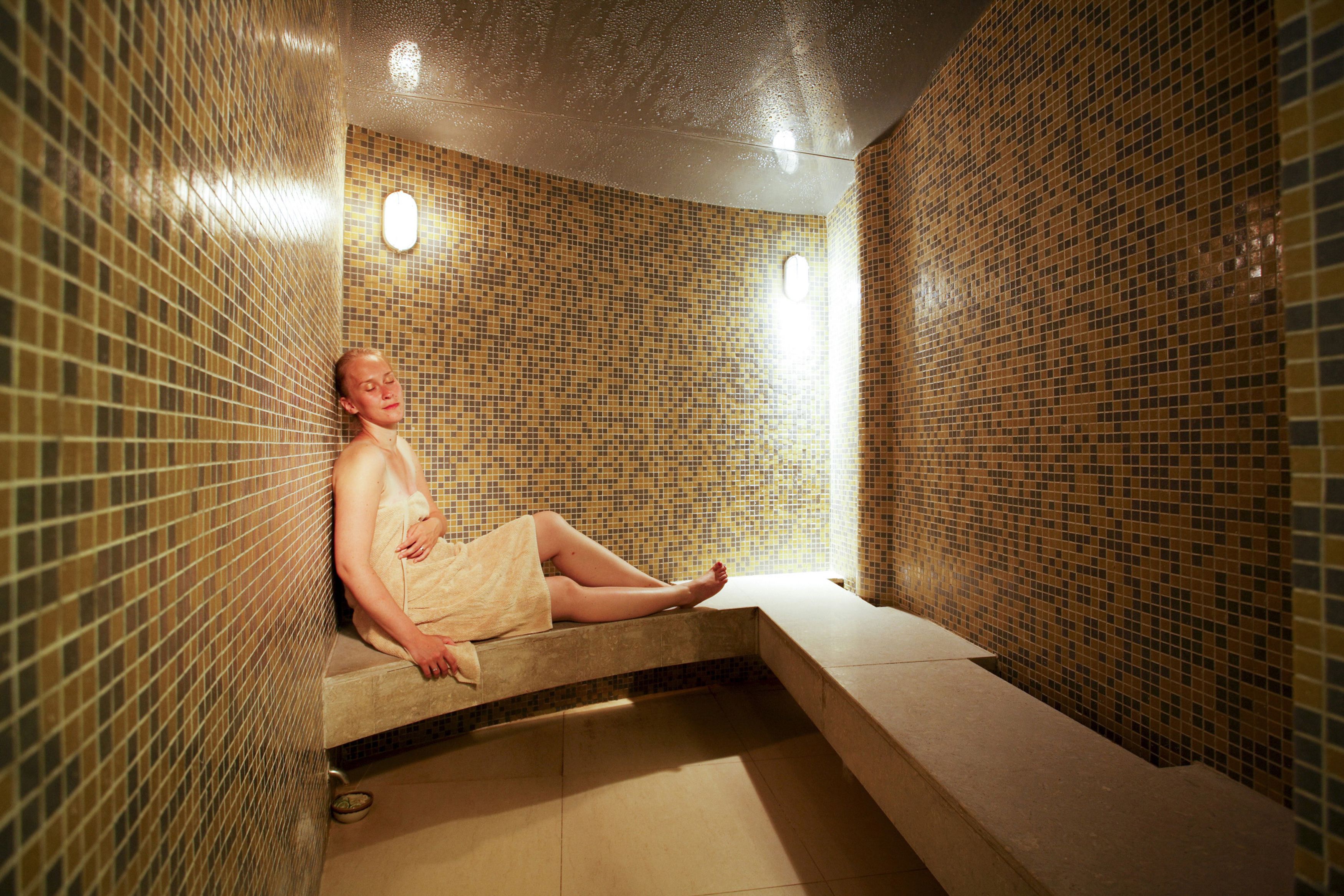 A person sitting in a tiled room with a bench and a small table.