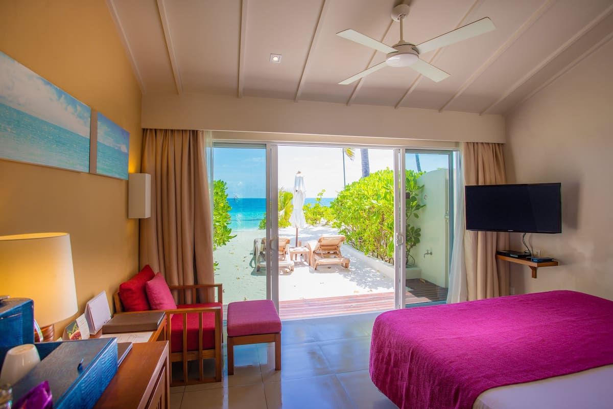 Habitación de hotel con cama, escritorio con silla, televisión y balcón con vistas a la playa y al océano.