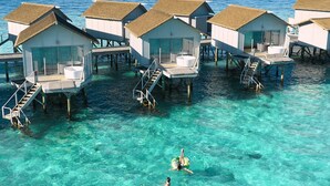Cabañas sobre el agua con agua azul cristalina y una persona nadando.