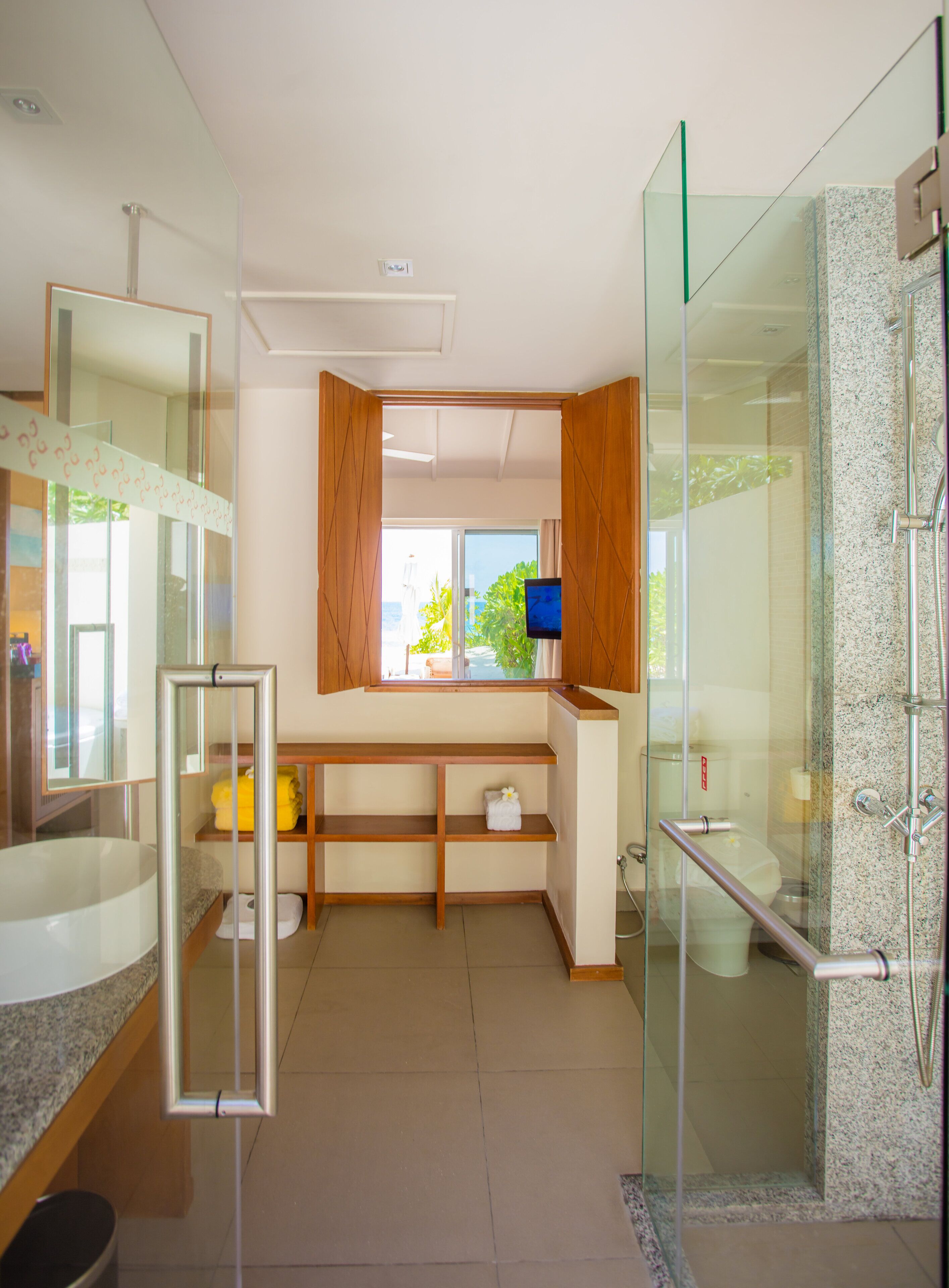 A modern bathroom with a glass shower enclosure, a large mirror, and a window with a view of greenery.