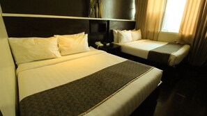 A hotel room with two beds, a bedside table with a phone, and a window with curtains.
