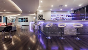Un espace bar moderne comprenant un comptoir, trois tabourets et un coin salon avec un canapé et des fauteuils.