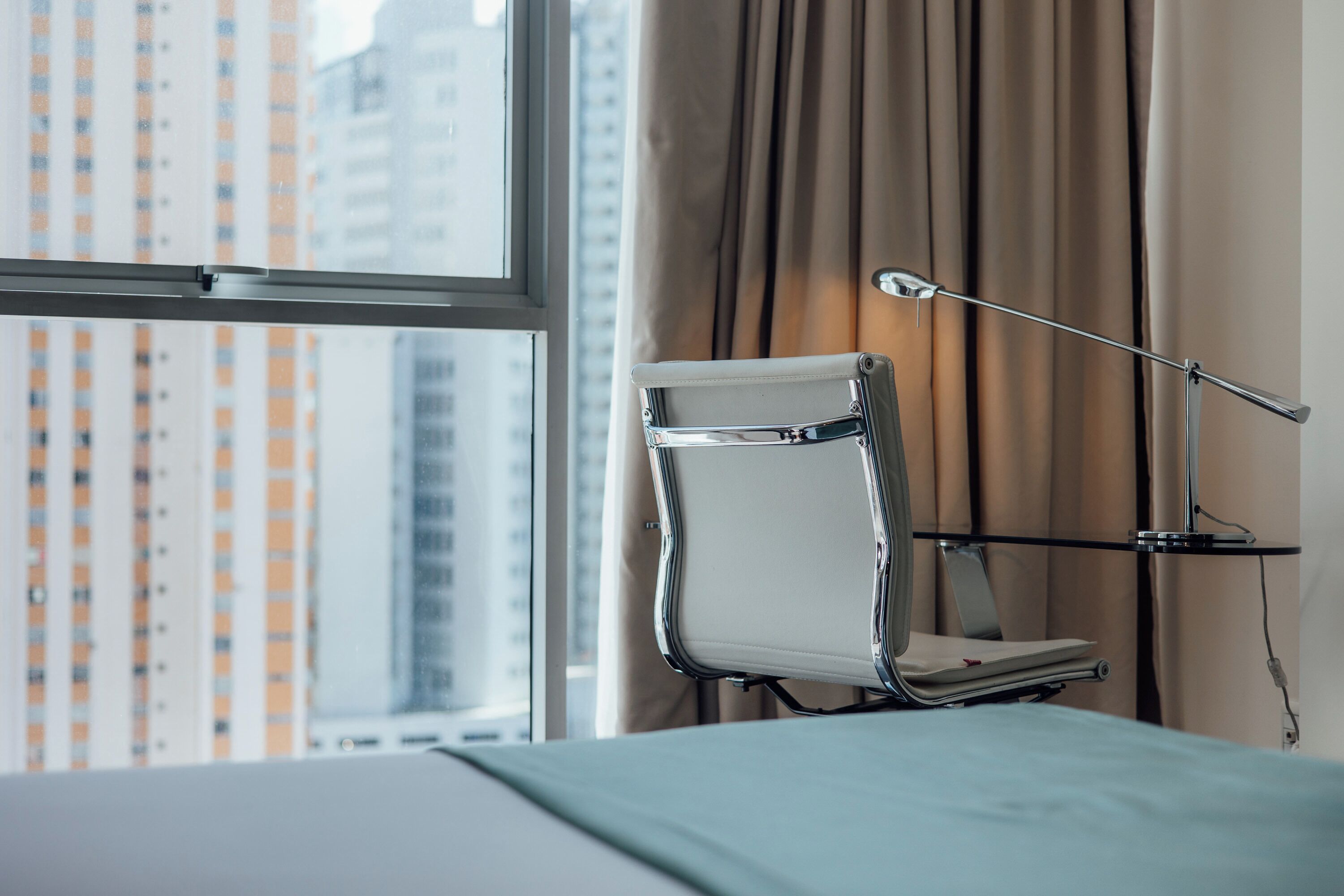 A hotel room with a bed, a bedside table, a lamp, and a window with curtains.