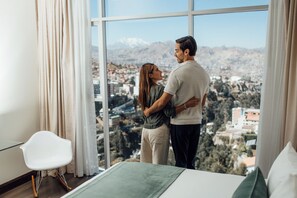 Una pareja de pie junto a una ventana con vistas a un paisaje urbano montañoso.