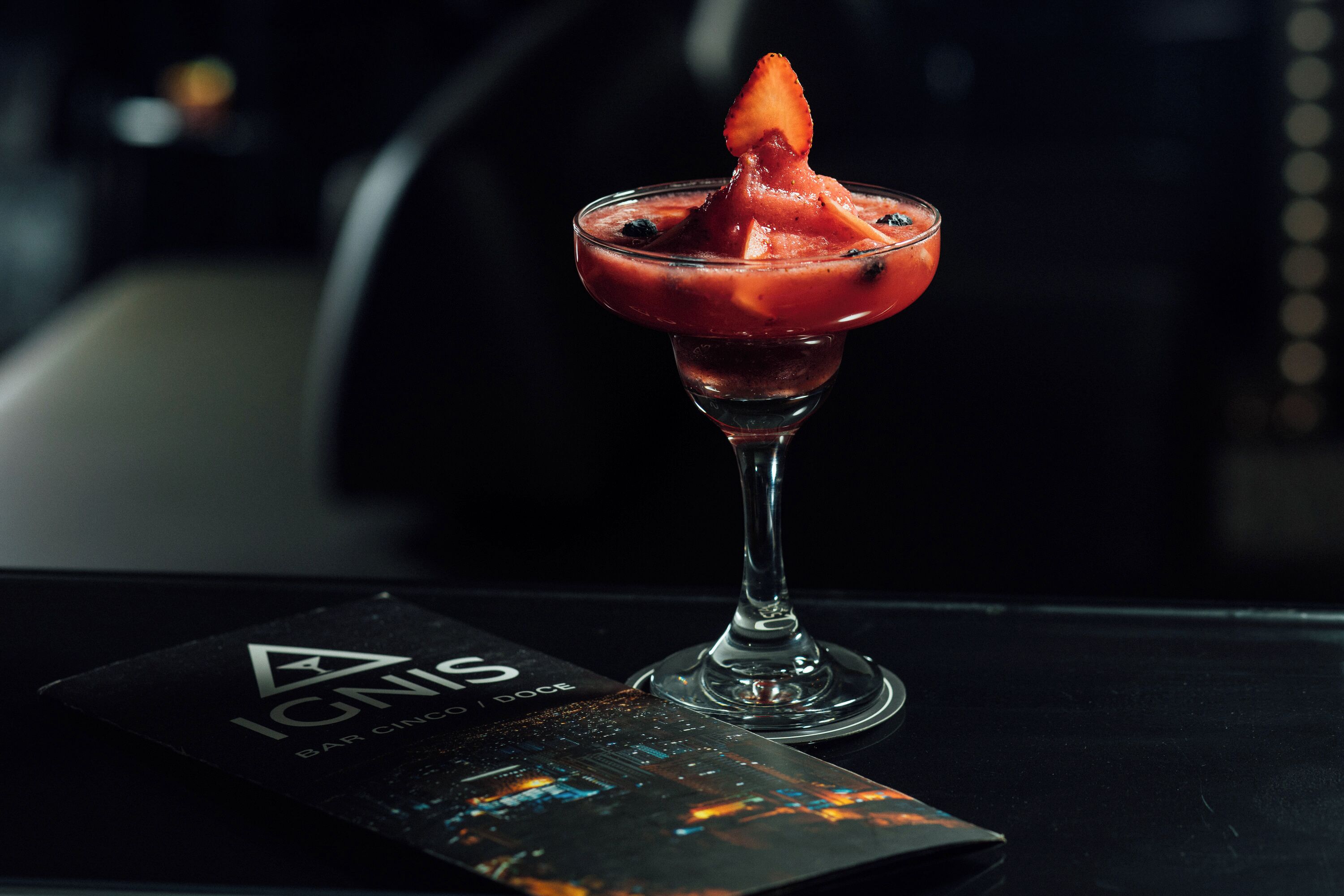 A cocktail in a martini glass with a strawberry garnish on a table with a menu.