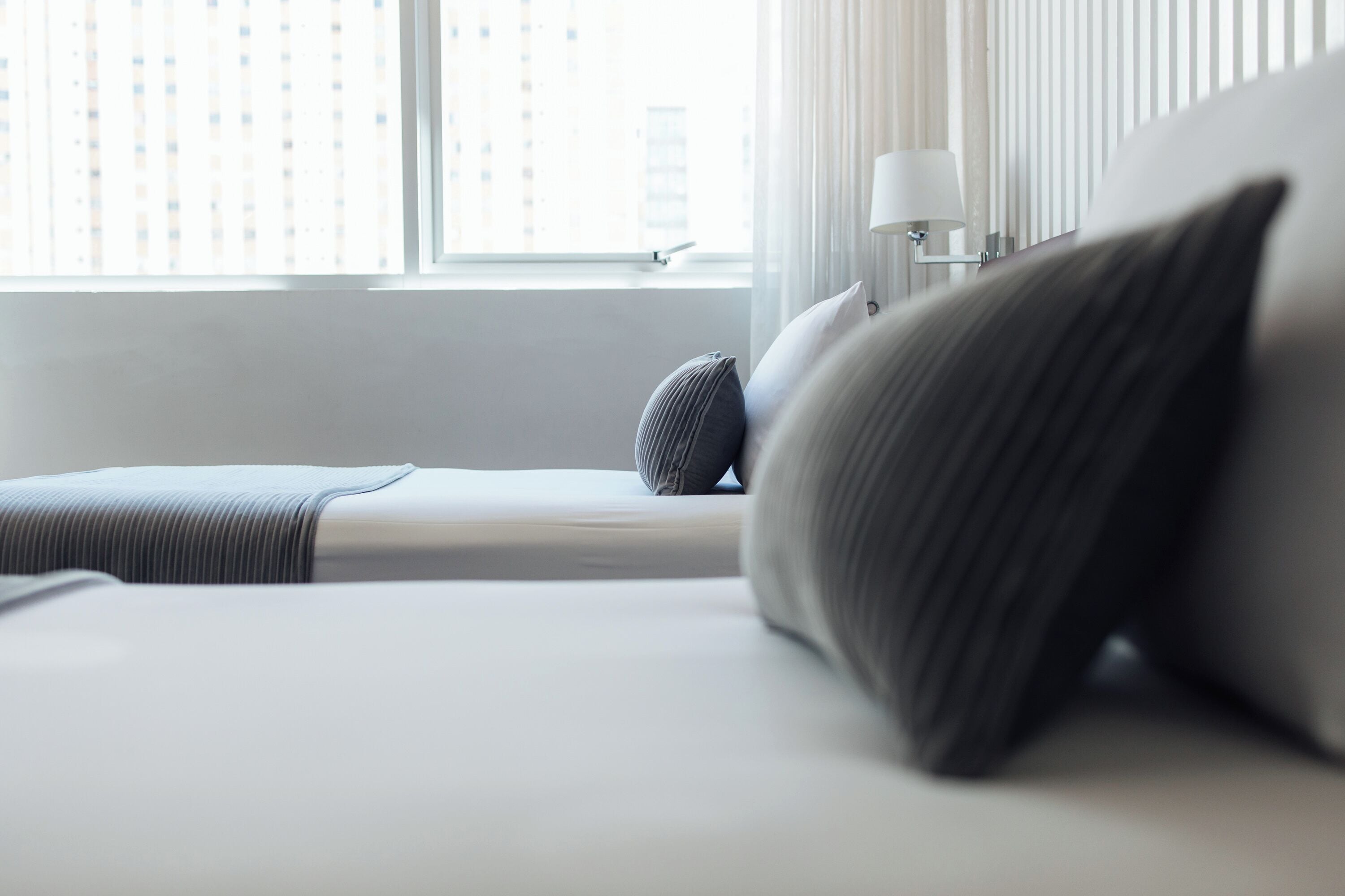 Ein modernes Hotelzimmer mit einem großen Bett, einem Nachttisch mit Lampe und Blick auf Gebäude durch das Fenster.