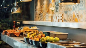 Un buffet proposant une variété de fruits et de plats, notamment des pommes et des bananes, éclairé par des lampes suspendues.