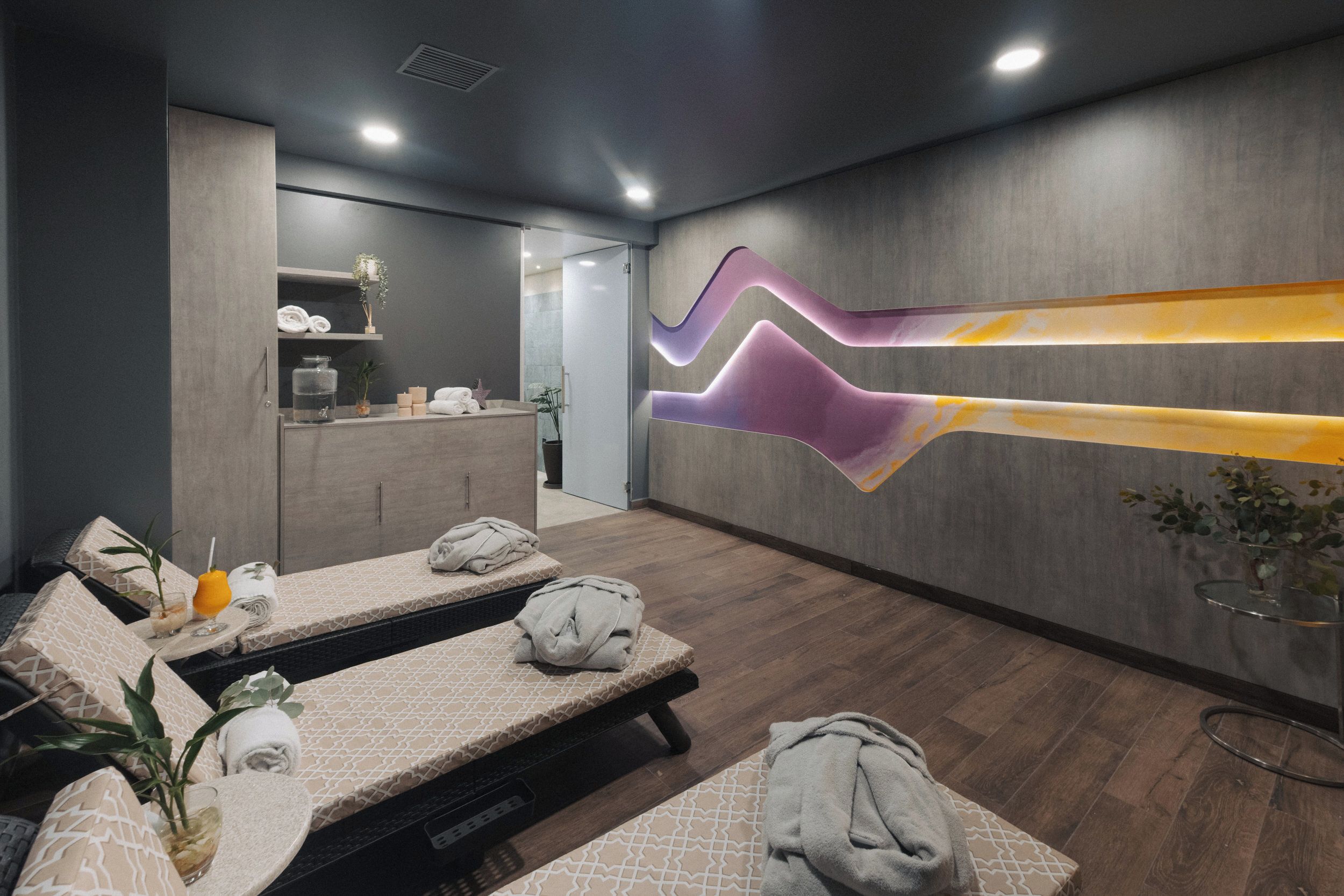 Un espace de spa moderne comprenant un comptoir d’accueil, des tables de massage et un élément décoratif mural.