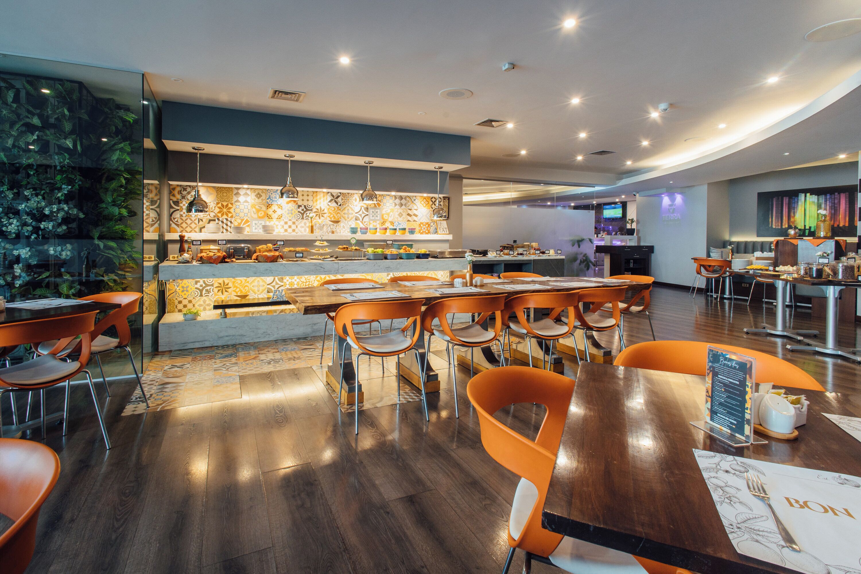 Un restaurante moderno con barra central, sillas naranjas y suelo de madera.