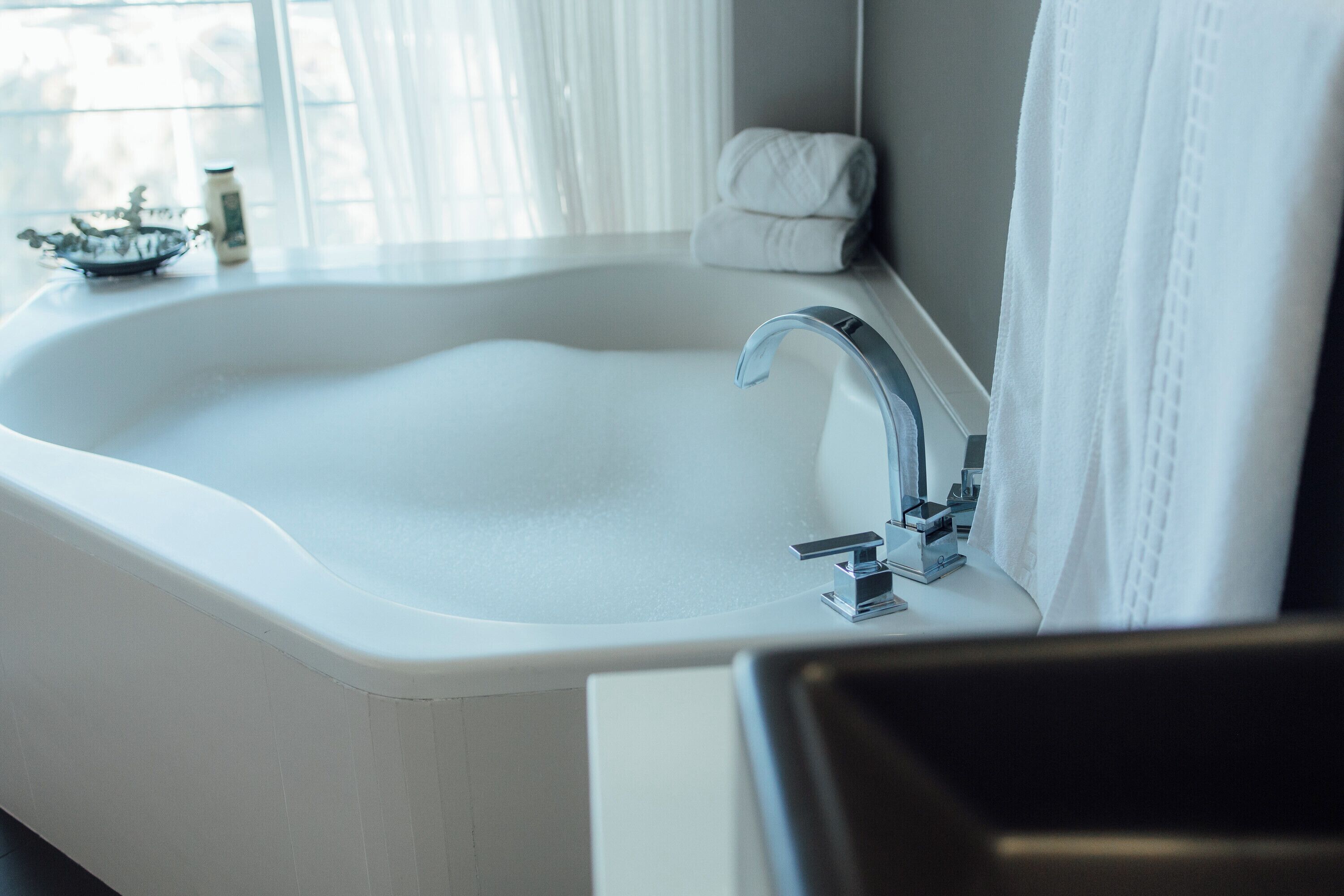 Un baño moderno con un lavamanos grande de color blanco, un grifo cromado y una ventana con cortinas traslúcidas.